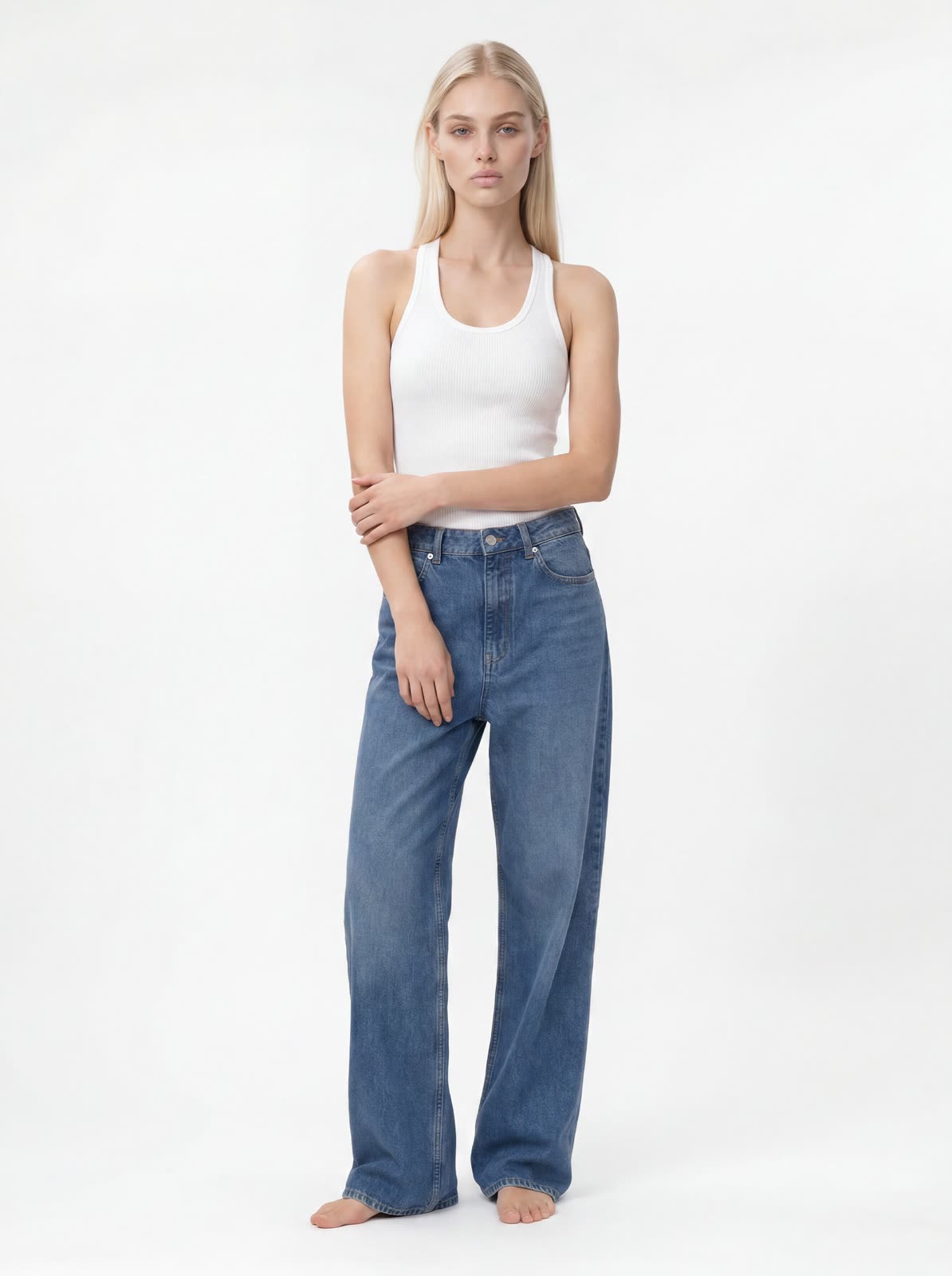 AI fashion model in a white ribbed tank top and blue wide-leg jeans, standing against a plain white studio backdrop